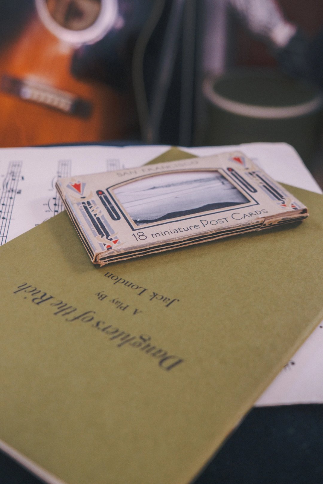 A stack of vintage postcards and a book with a green cover, set against a blurred background of a guitar.