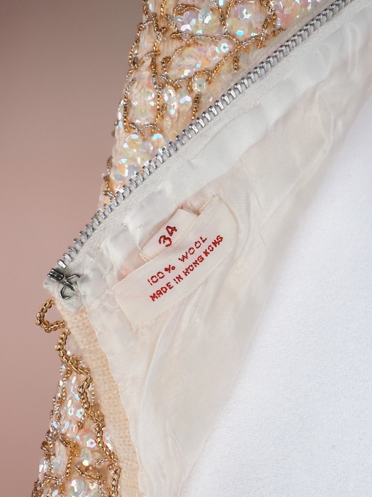 White 1960s women's top with a sparkling floral design and a tag indicating 100% wool, made in Hong Kong.