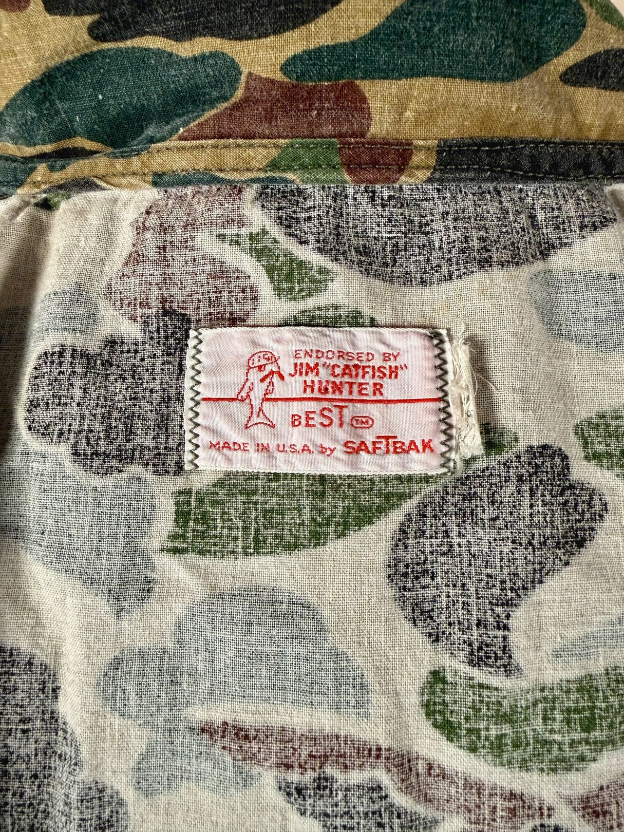Camo jacket featuring a 1970s design, with predominant camouflage green colors and an endorsement tag for Jim "Catfish" Hunter.