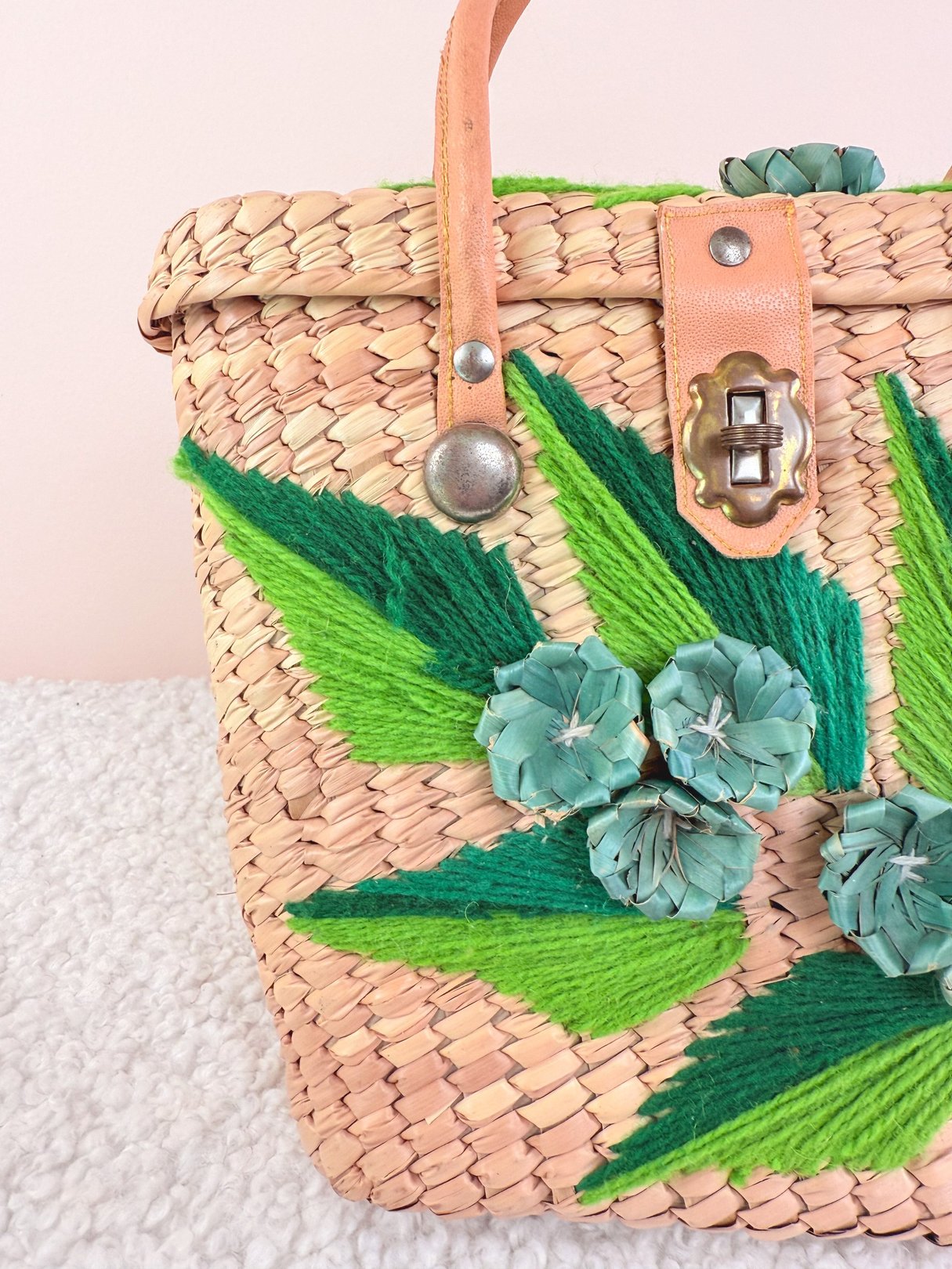Woven straw handbag featuring blue and green floral embellishments, with a tan leather strap and a 1970s design, ideal for women's accessories.