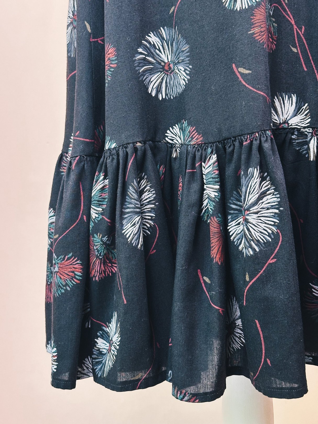 Black ruffle skirt with a floral dandelion print, featuring a tiered hem and 1970s era design for women.