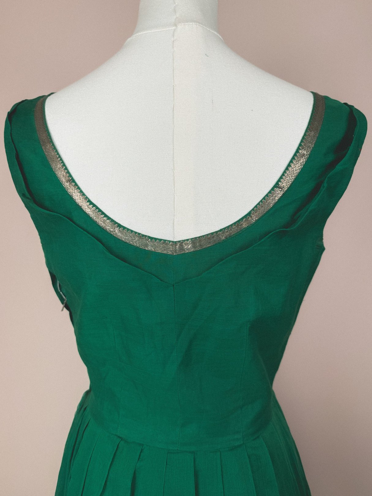 The back of a 1950s women's dress in emerald green featuring a deep scoop neckline trimmed with metallic gold detailing.