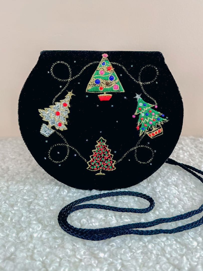 A round black velvet purse featuring colorful embroidered Christmas tree designs, with a braided strap.