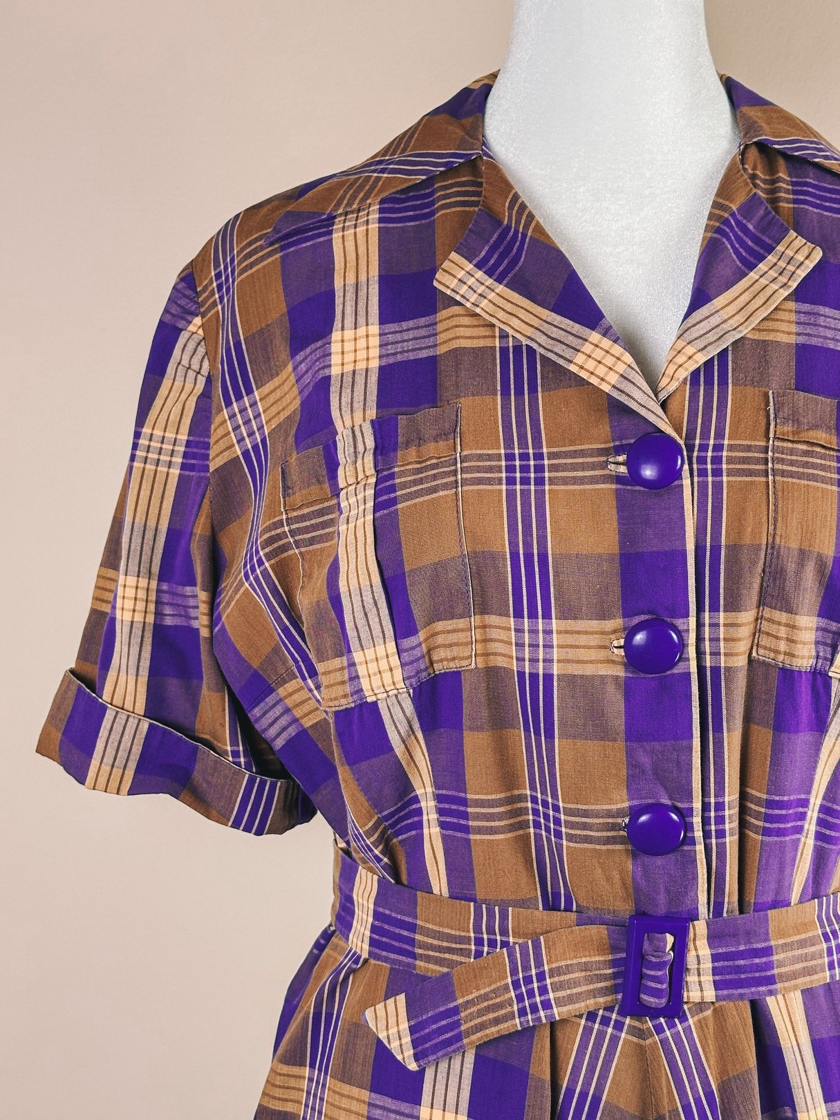Purple plaid dress with a collar, short sleeves, and large buttons, featuring a fitted waist and a subtle belt detail.