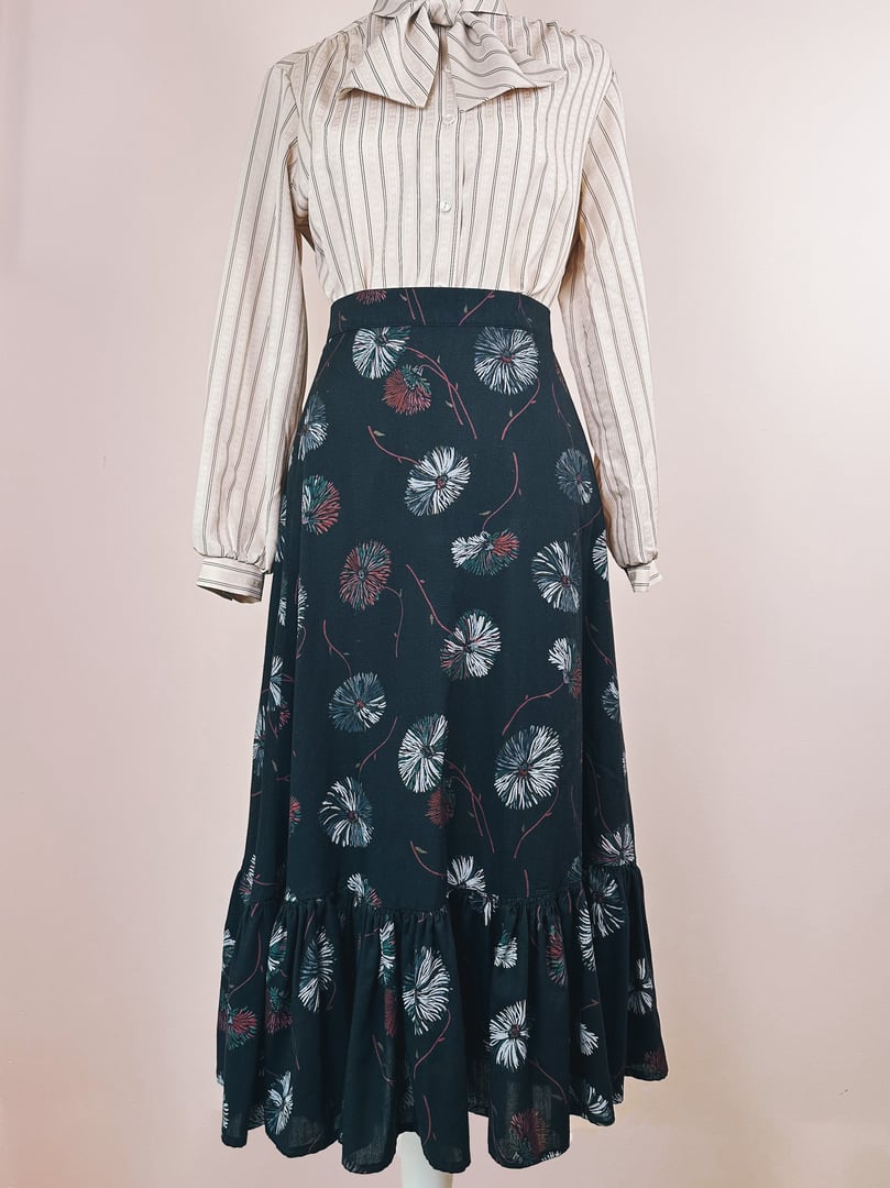 Black Dandelion Ruffle Skirt featuring a flower pattern, styled with a striped blouse, from the 1970s aimed at women.