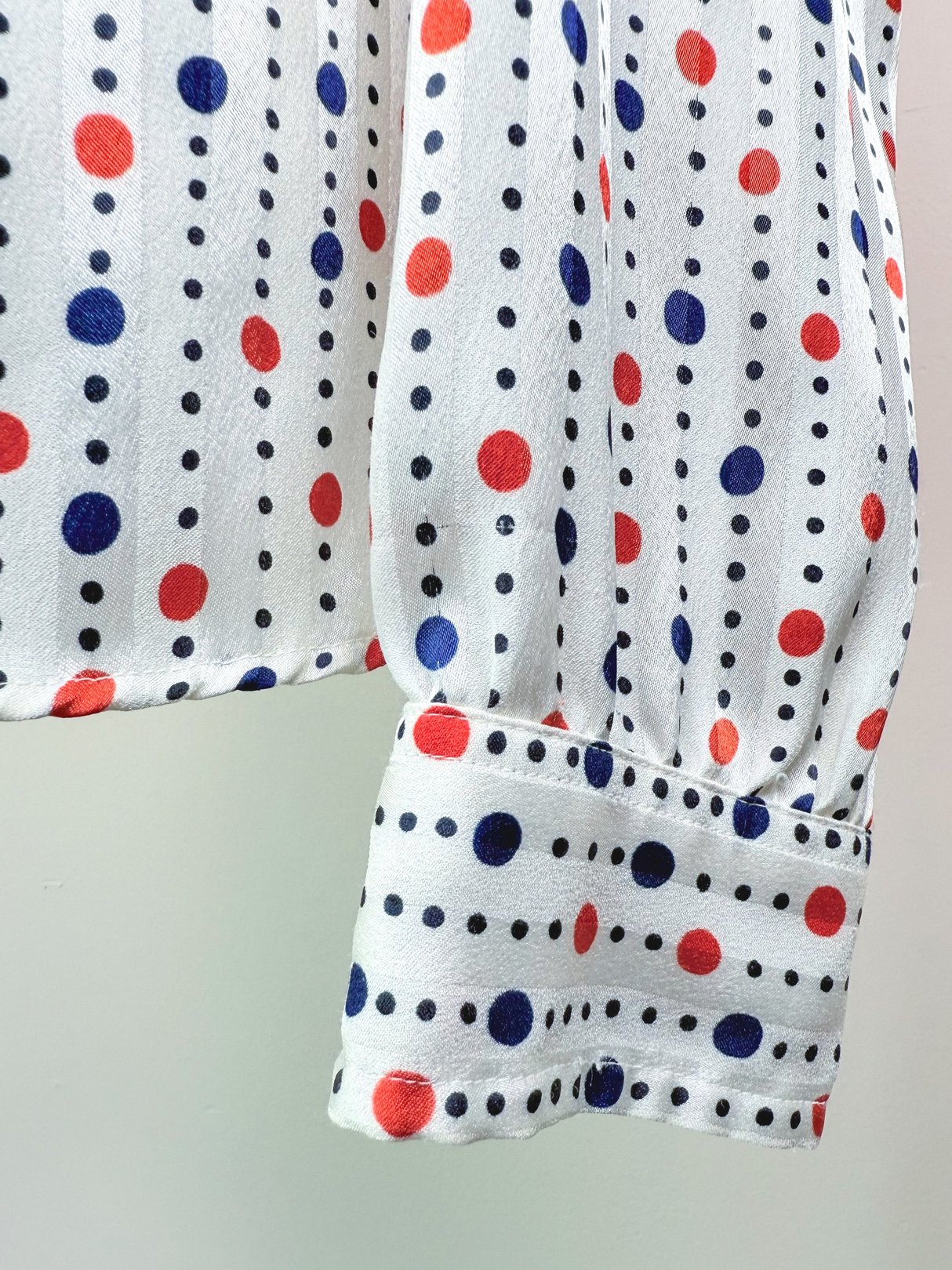 1980s women's blouse featuring a white fabric with red and navy polka dots and a gathered sleeve cuff.