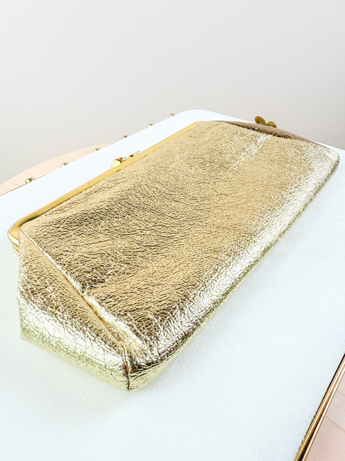 A gold, textured 1950s clutch bag designed for women, featuring a sleek rectangular shape and a secure clasp closure.