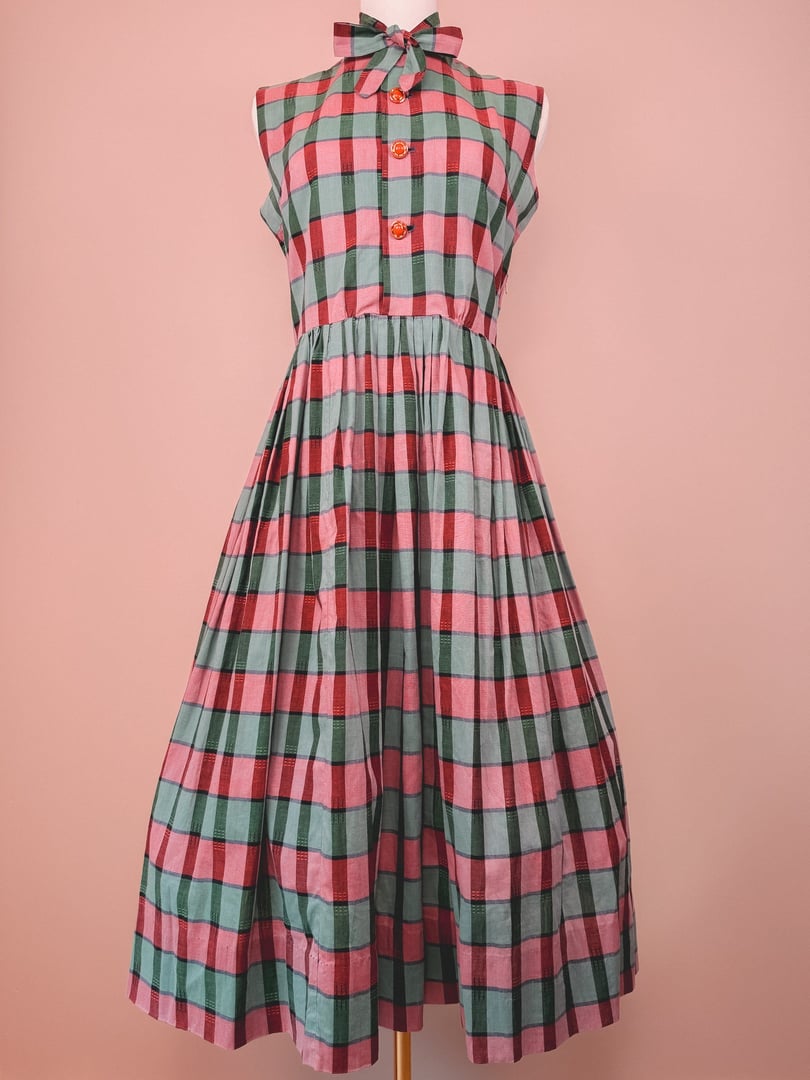 1950s women's red and green plaid dress featuring a button-up front and a bow tie collar.