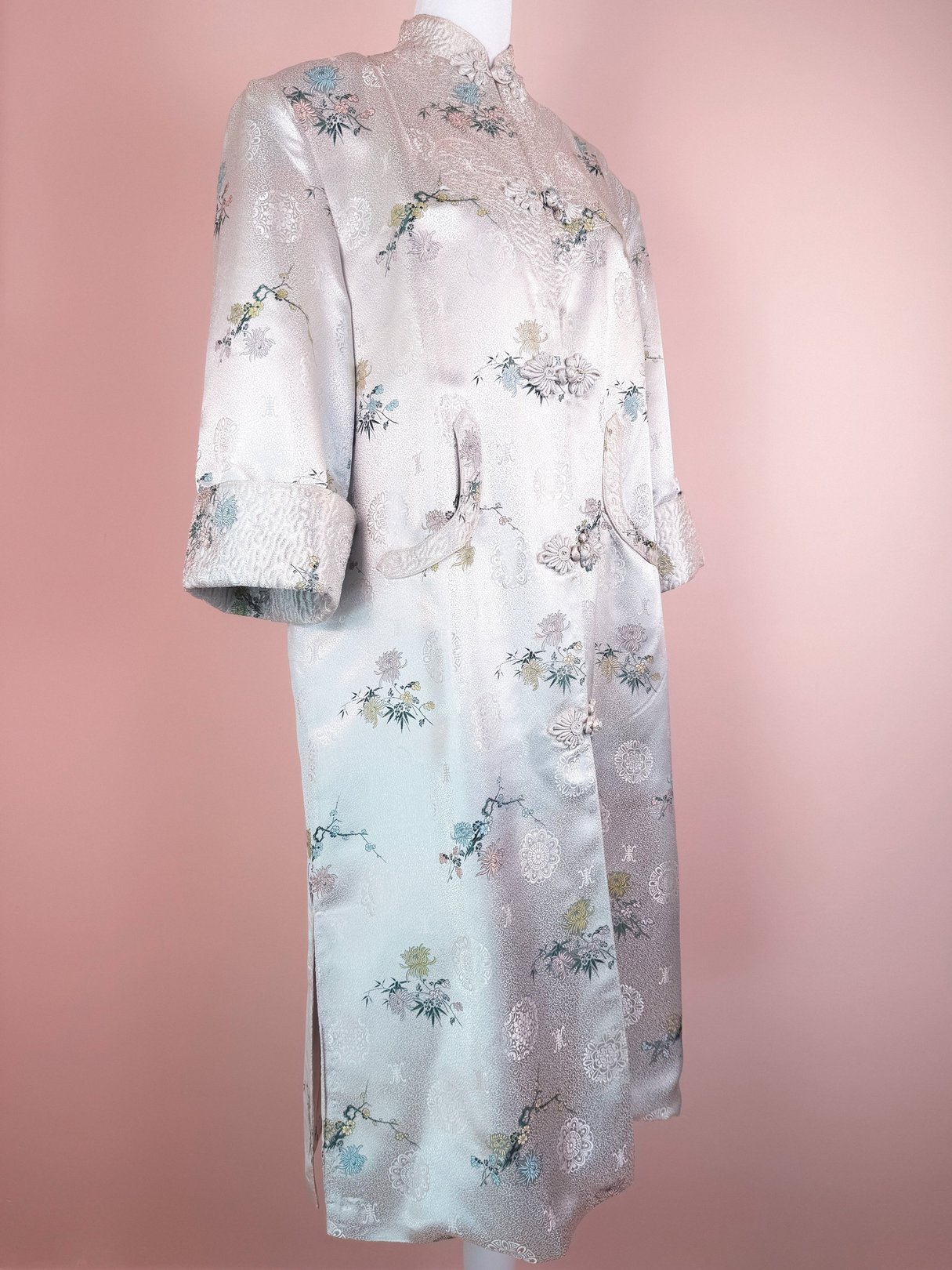 Silver 1970s women's cheongsam coat featuring floral patterns, long sleeves, and side slits.