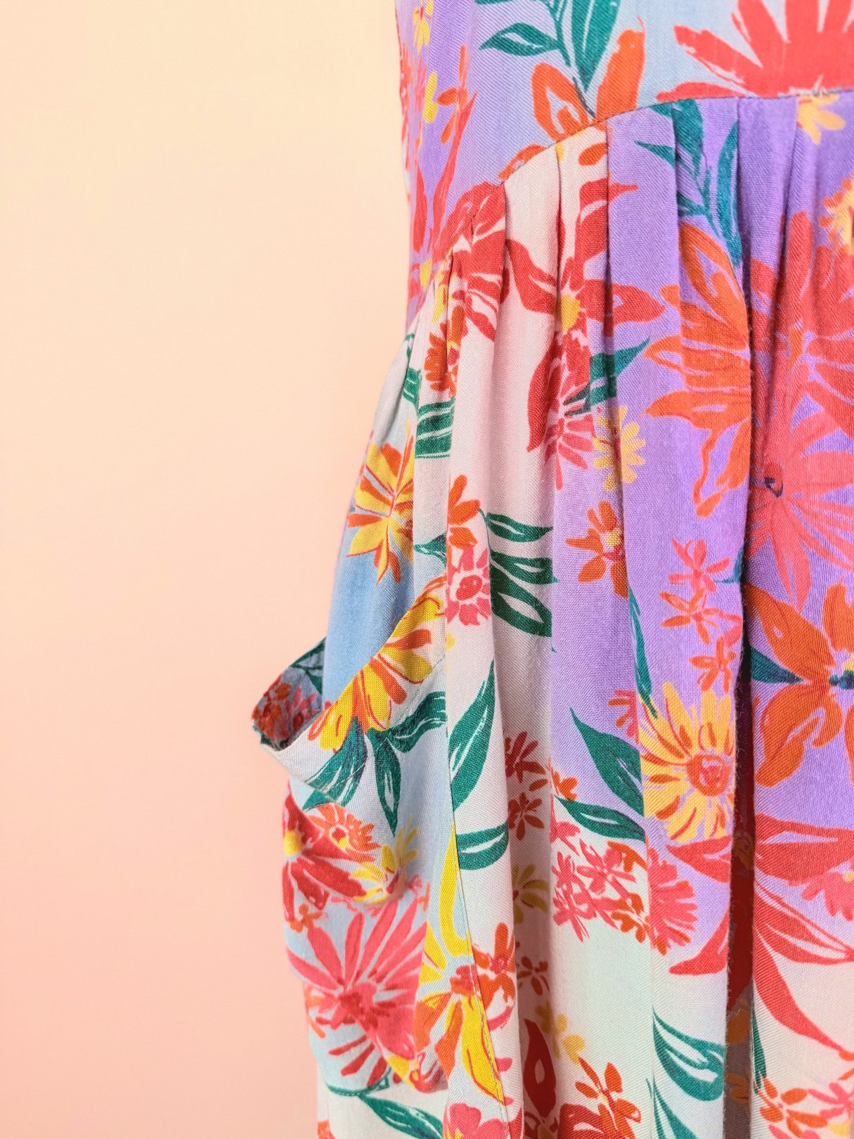 A colorful 1990s women's dress with a floral pattern features pink, orange, and green hues and includes a side pocket.