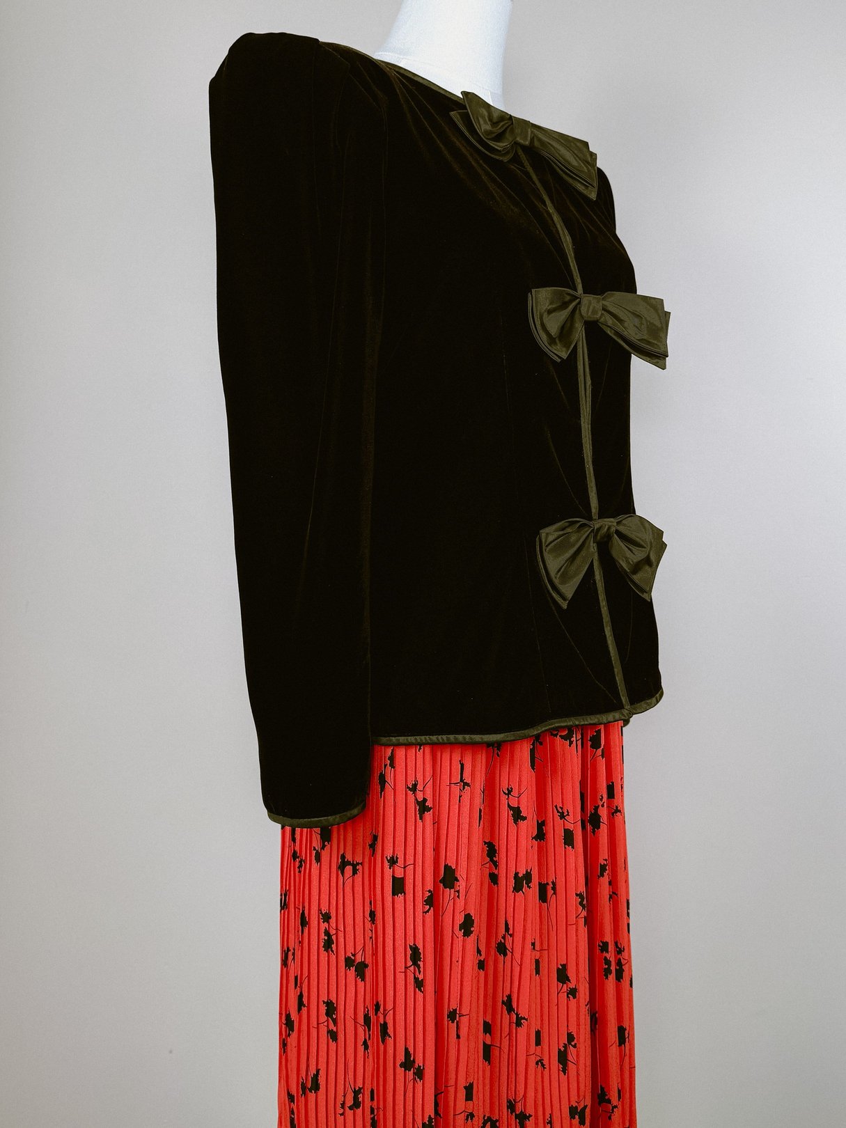 Black velvet 1980s women's jacket featuring three decorative bows, styled with a red floral-printed skirt.