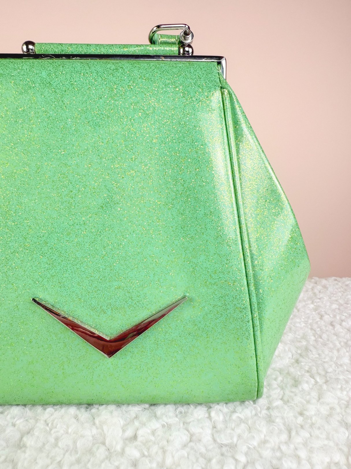 Sparkling mint green handbag with a structured shape and red accent detail, reflecting a 1950s style.