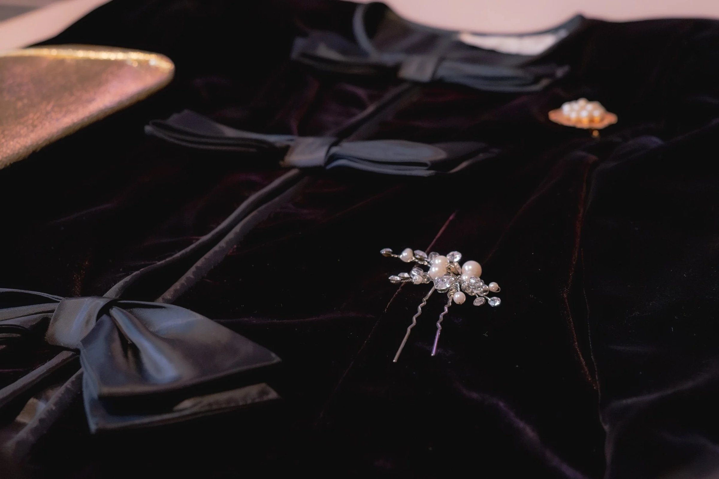 A close-up of a velvet garment featuring an ornate hairpin embellished with pearls and crystals.