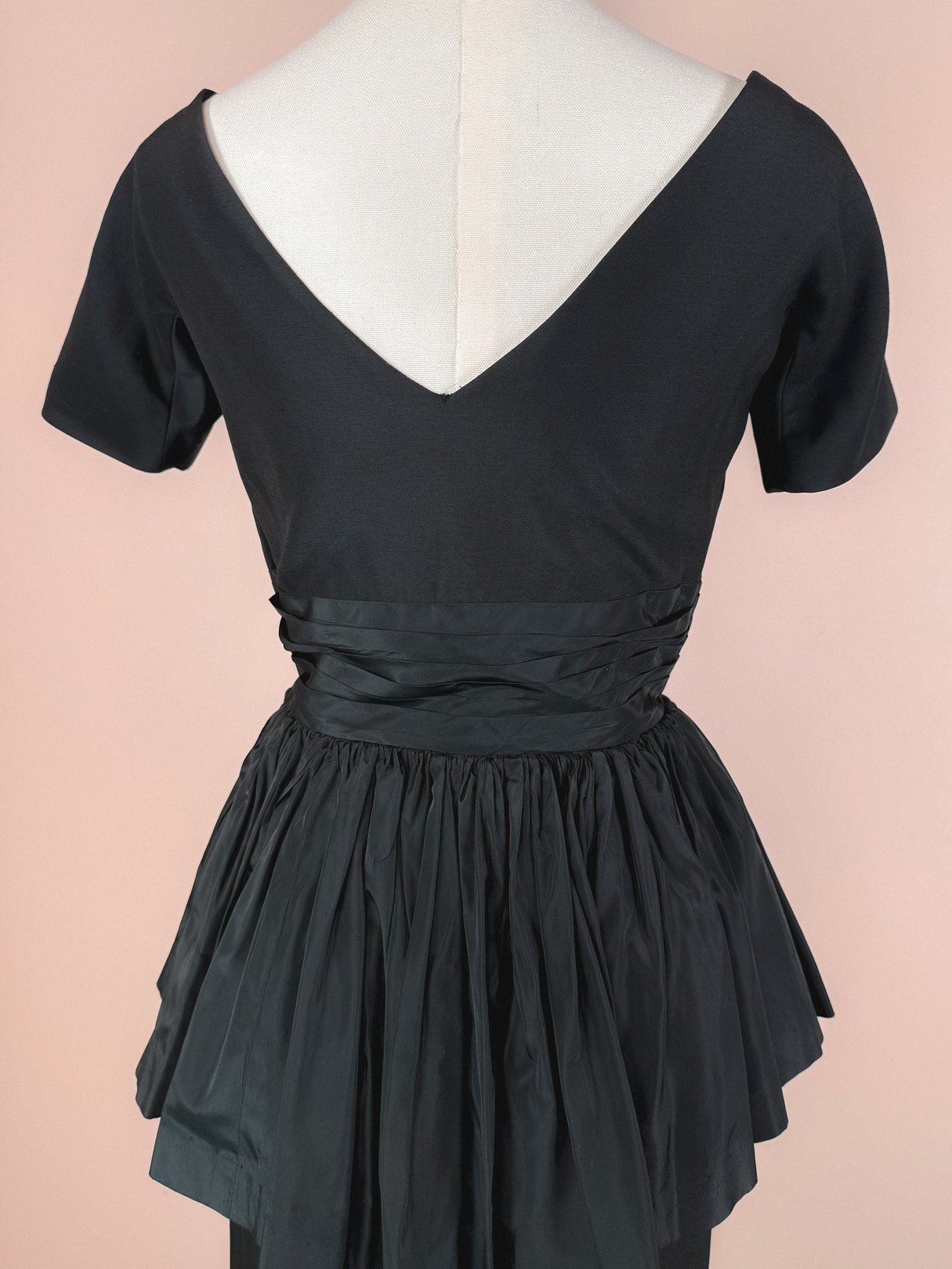 The New Years Starlet Dress is a vintage-style 1950s women’s dress in black, featuring a fitted bodice and a full, gathered skirt with a sash detail at the waist.