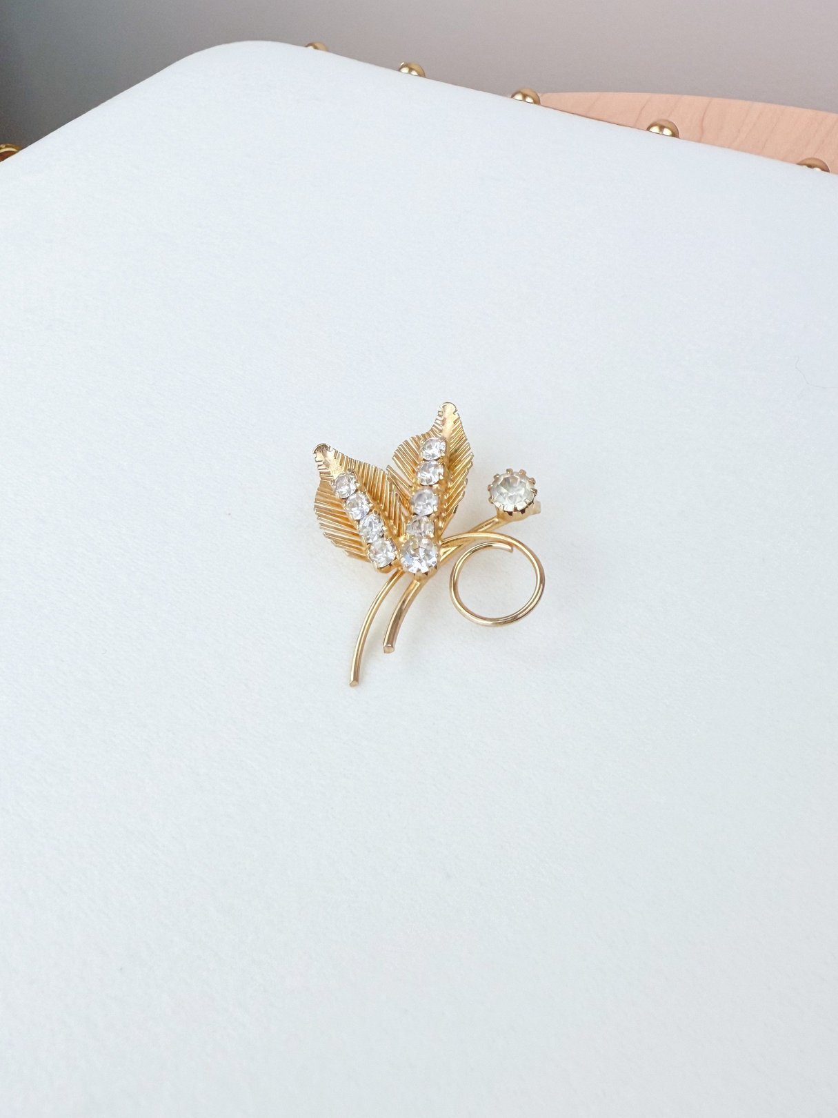 A gold tone brooch designed as a fern with sparkling rhinestones and a circular accent, characteristic of 1950s women’s jewelry.