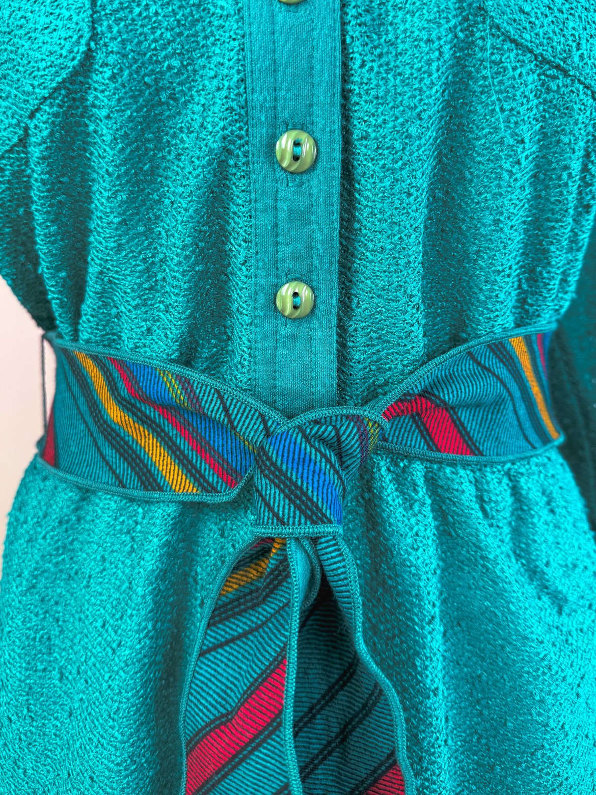 Teal dress with a textured fabric, featuring a button-up front and a multicolored striped tie belt.