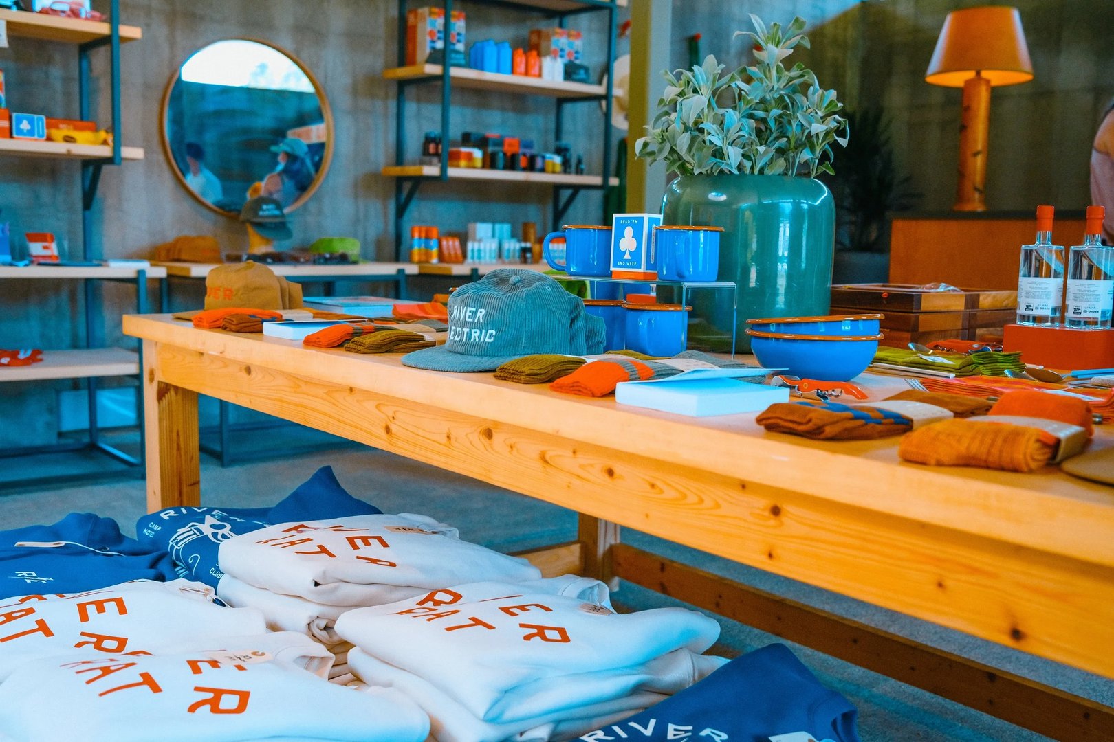A display of various apparel and accessories, including hats, mugs, and sweatshirts, arranged on a wooden table in a brightly lit store.