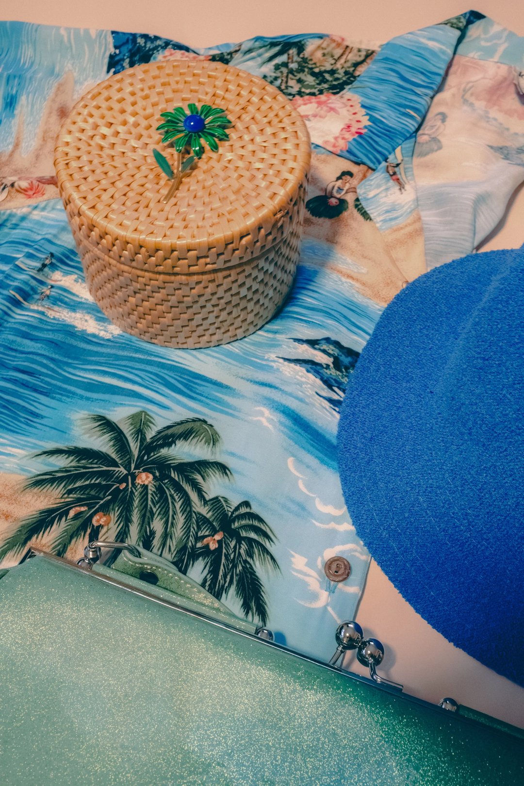 A colorful beach scene featuring palm trees, a textured woven basket, and a blue cap.