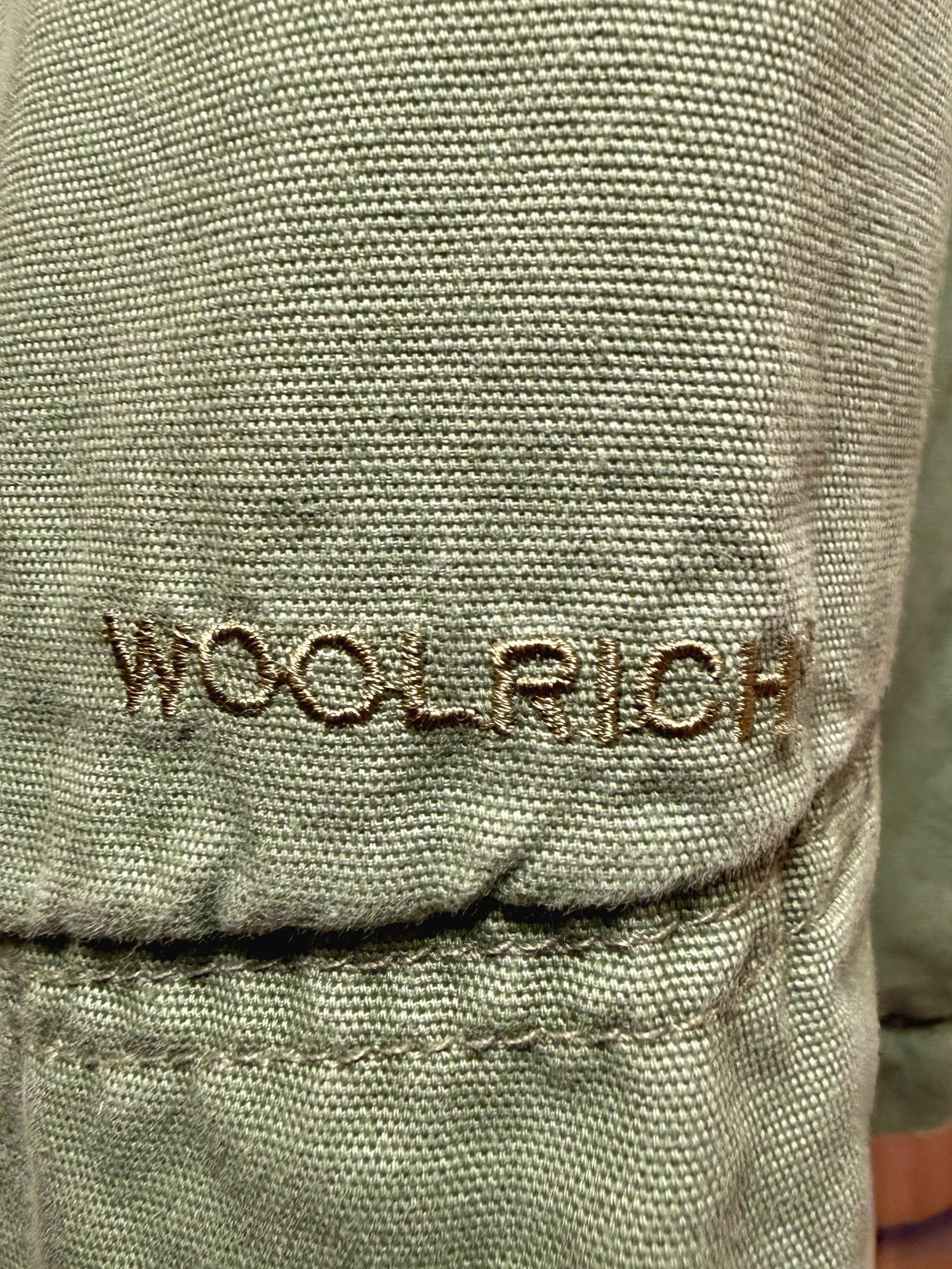 Sage Quilted Woolrich Jacket featuring the brand name "Woolrich" embroidered on the fabric.