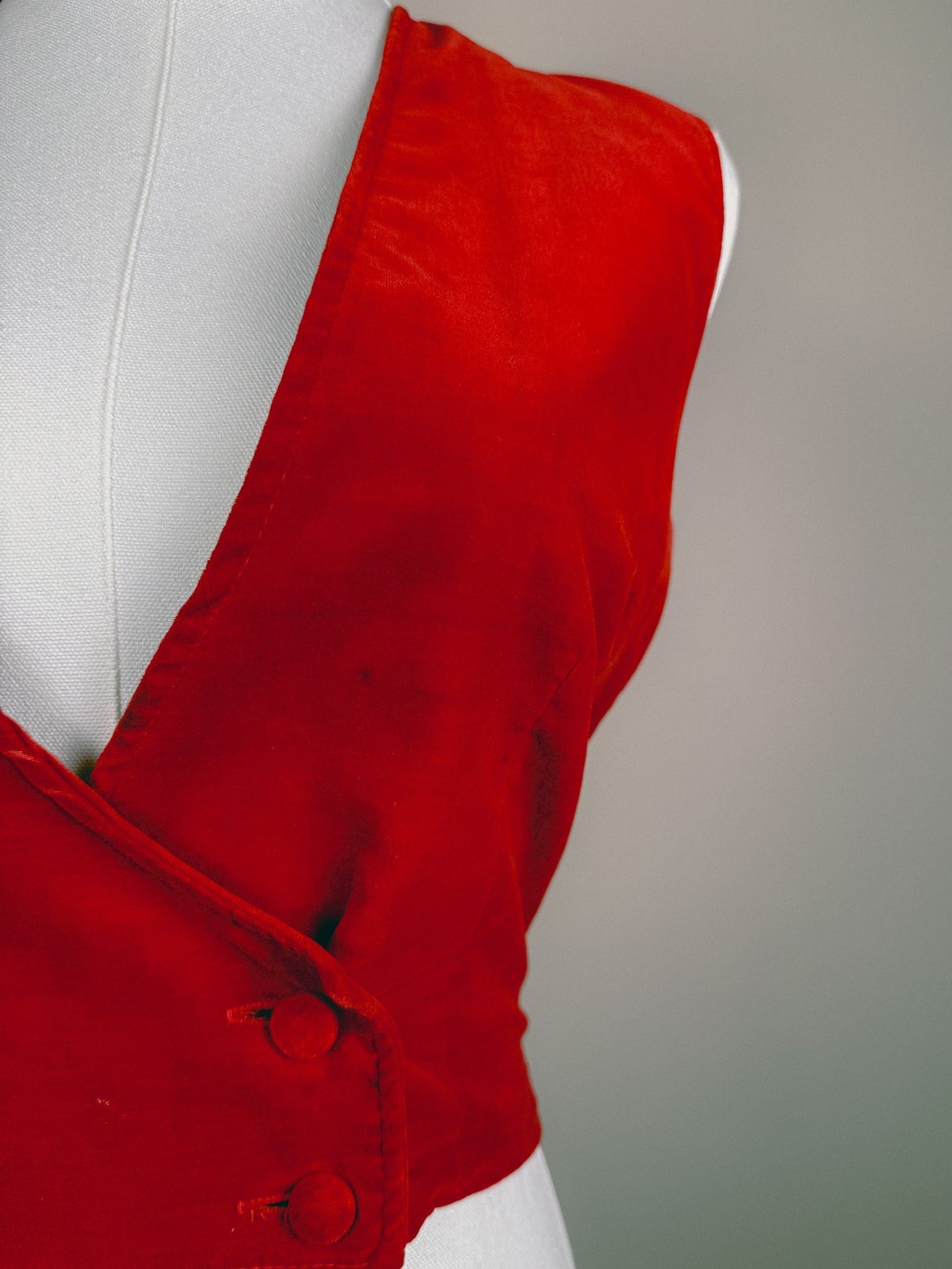 Red velvet sleeveless vest with a deep V-neck and two buttons, reflecting a 1970s style for women.