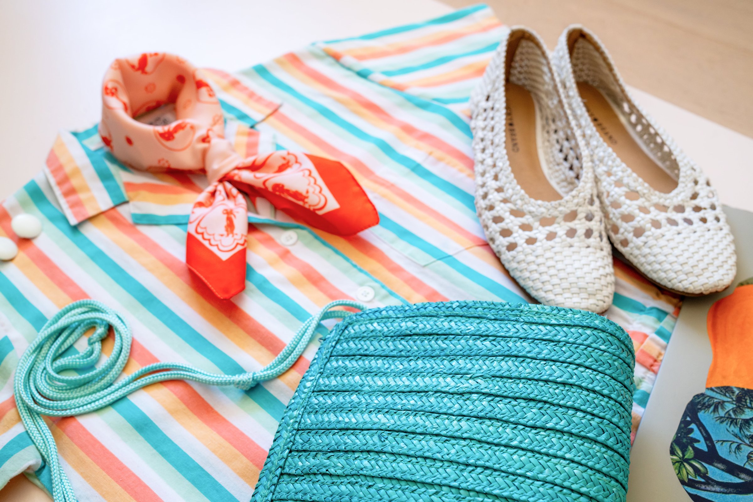 Inspired by Summer, Styled by Music gallery image: A striped short-sleeve shirt in pastel colors, a red and orange scarf, woven white slip-on shoes, and a turquoise braided handbag are arranged together.