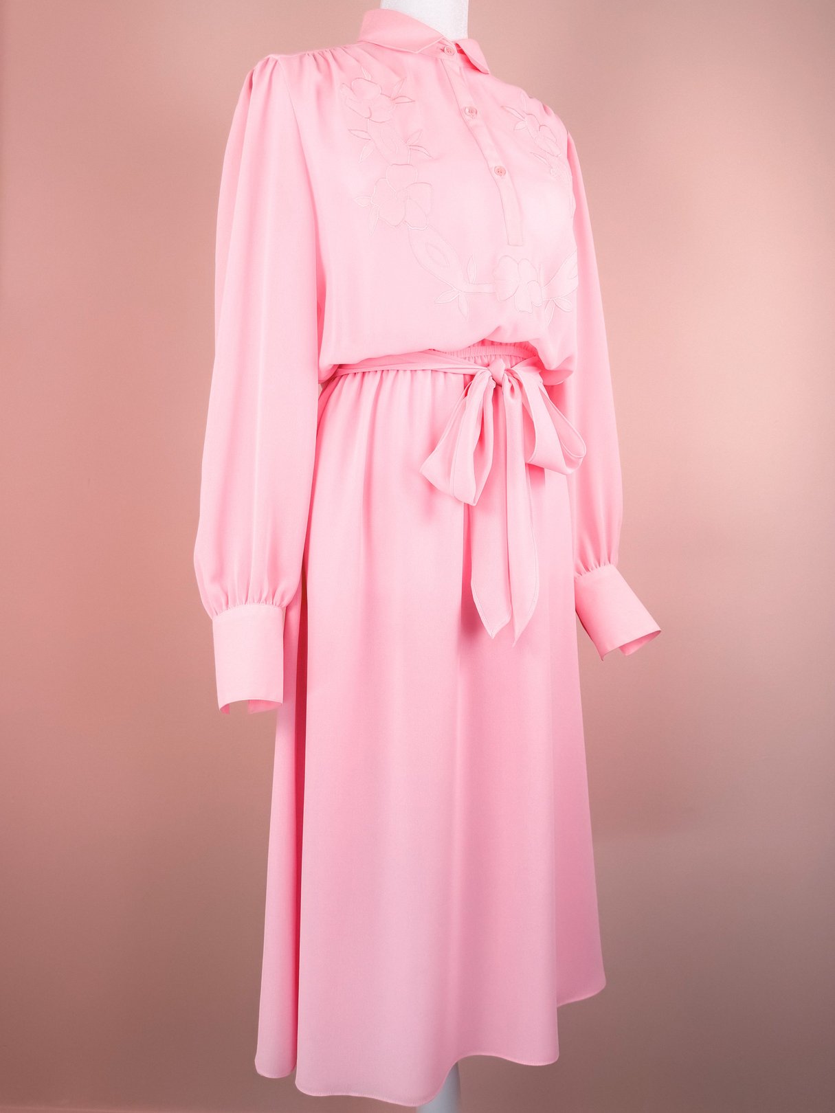 Bubble gum pink 1980s women's dress featuring long sleeves, a buttoned front, and a belted waist with floral embroidery.