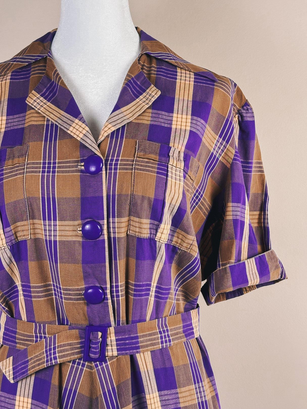 Purple plaid dress featuring a collared neckline, short sleeves, and a belted waist, reflective of 1950s fashion.