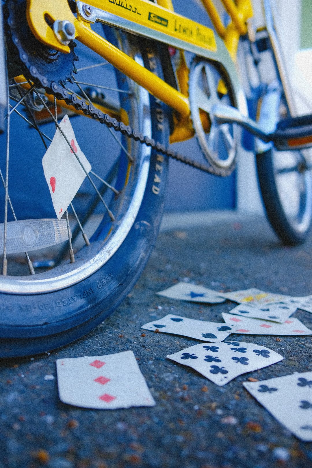 A close-up of a yellow bicycle with playing cards scattered on the ground beside it.