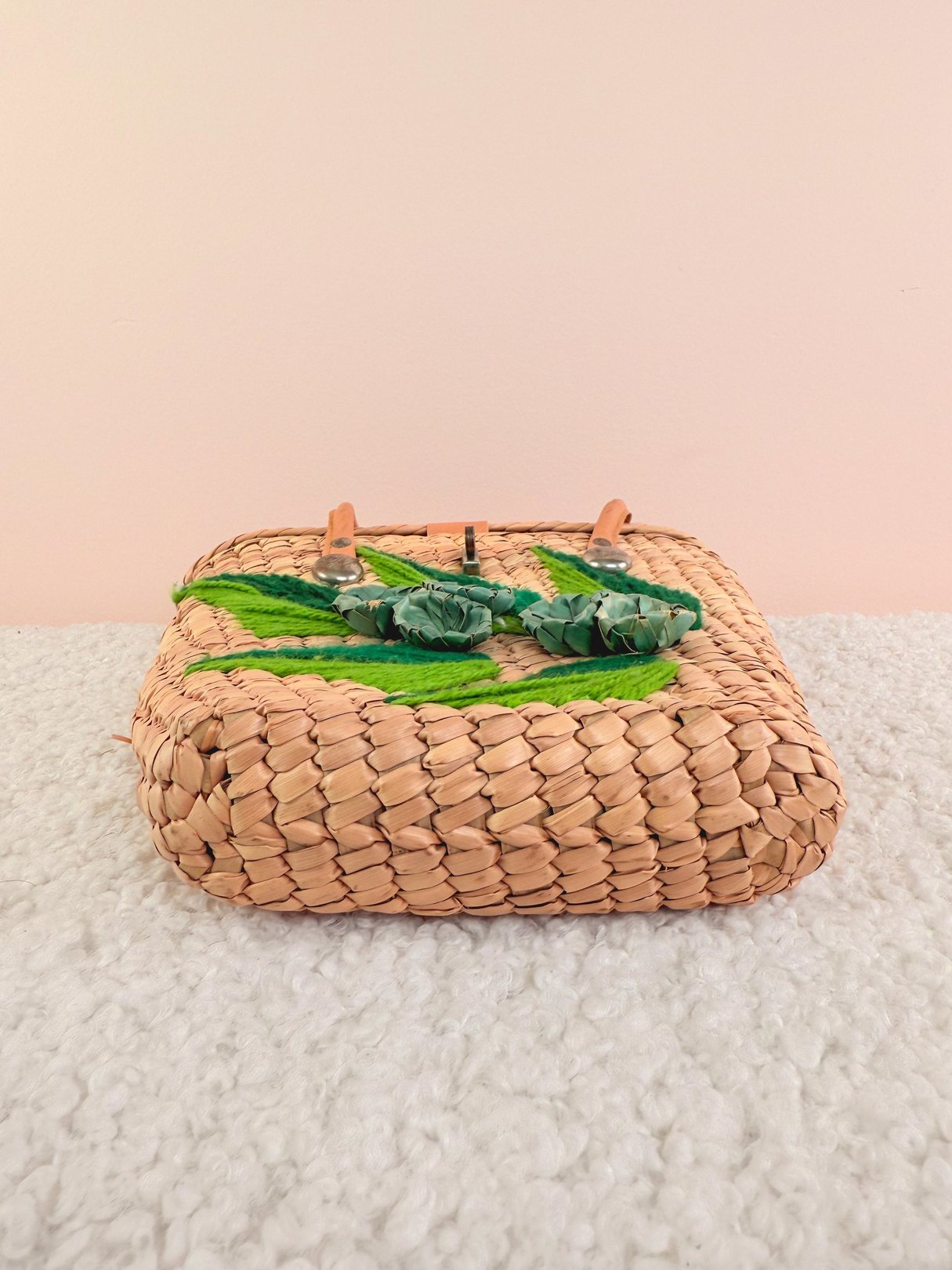 The On Vacation Straw Handbag features a woven design with green leaf and floral embellishments, ideal for women's accessories from the 1970s in a natural color palette.