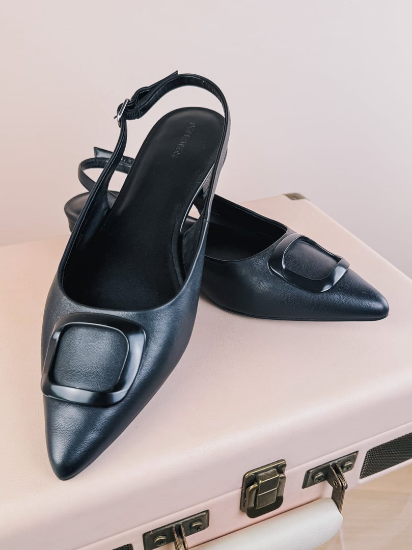 Black 1960s women's slingback flats featuring a pointed toe and a large square buckle detail.