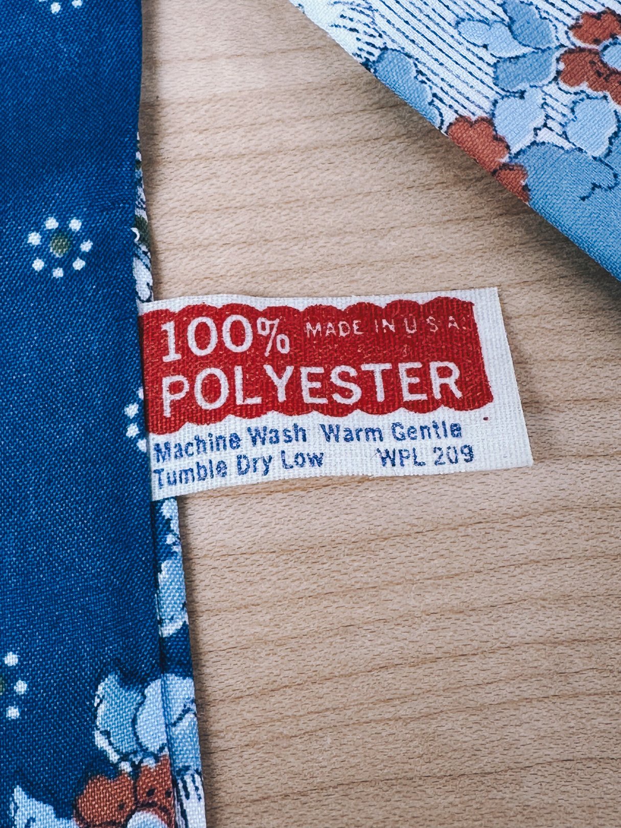 Light blue paisley scarf made of 100% polyester, featuring a care label indicating machine wash and tumble dry instructions.