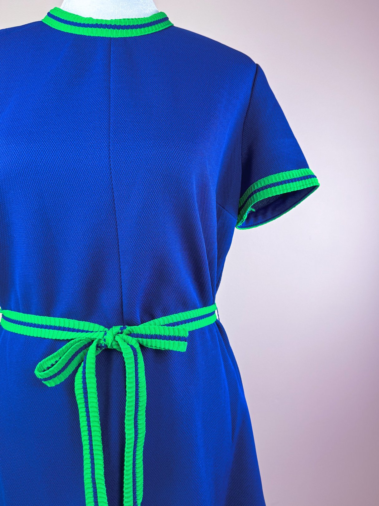 A 1970s women's dress in blue fabric featuring green striped trim and a matching belt.