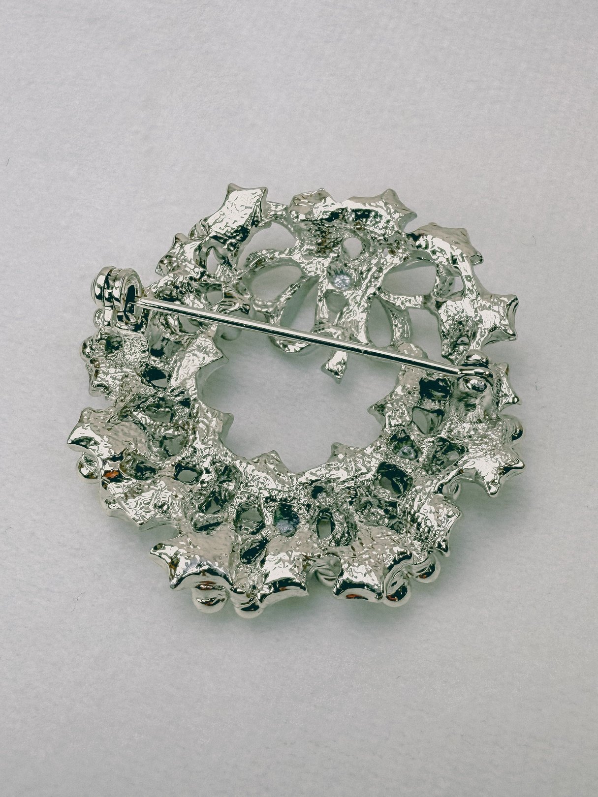 Silver 1970s keepsake wreath brooch with a textured design and a central floral motif.