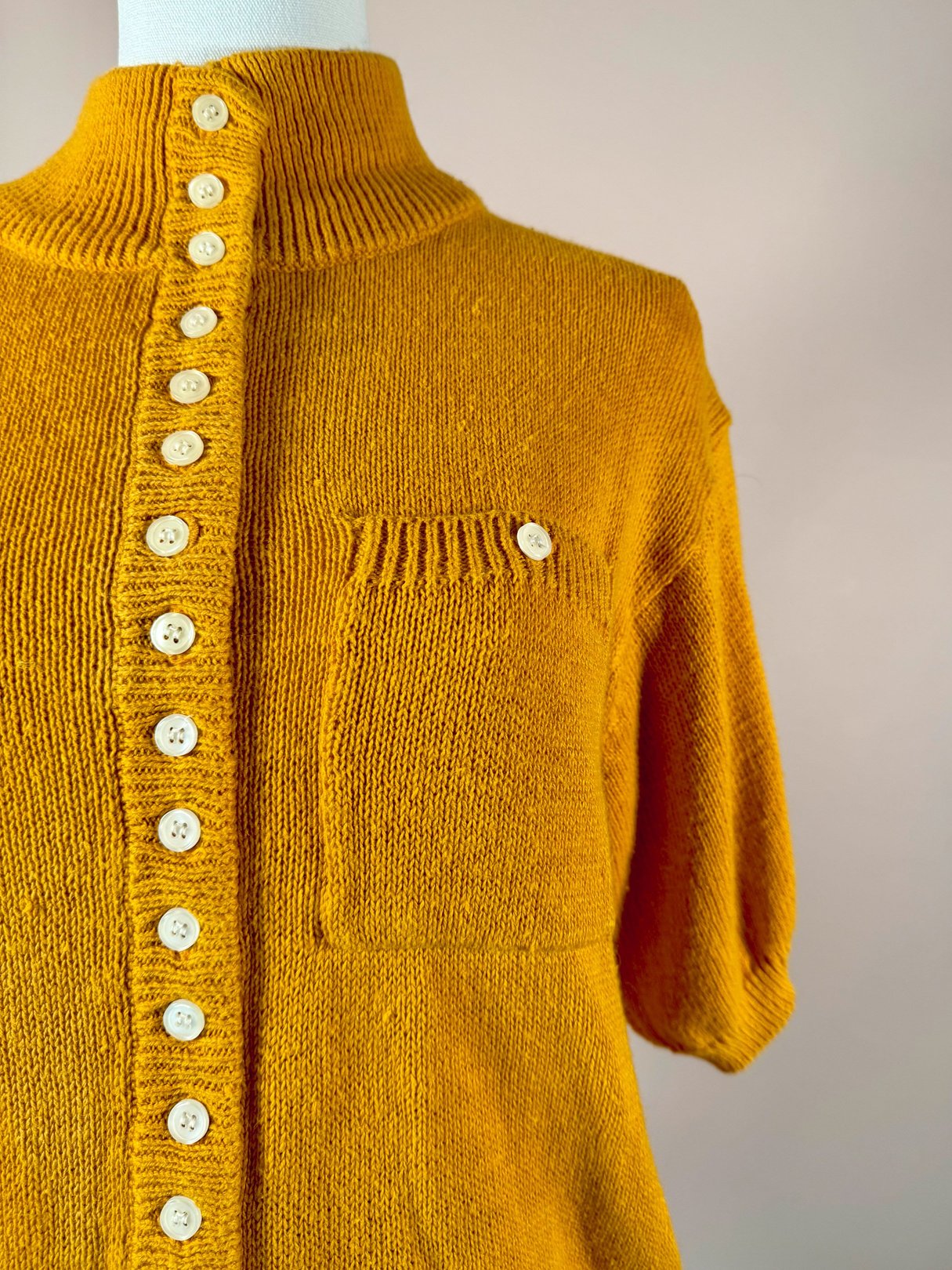 1980s vintage persimmon orange sweater for women featuring short sleeves, a collar, and a front pocket with button detailing.