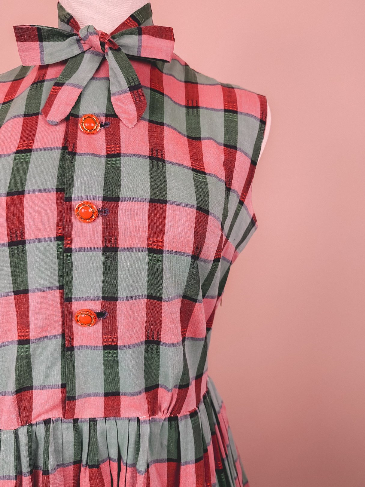 Red and green plaid dress with a bow neckline and orange buttons, reflecting 1950s women's fashion.