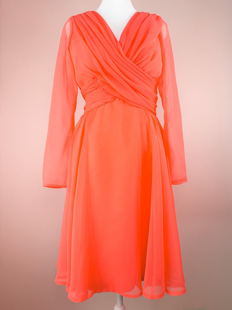 Coral Soirée Dress features a wrapped bodice with draped long sleeves and a flared skirt, reflecting 1960s fashion.