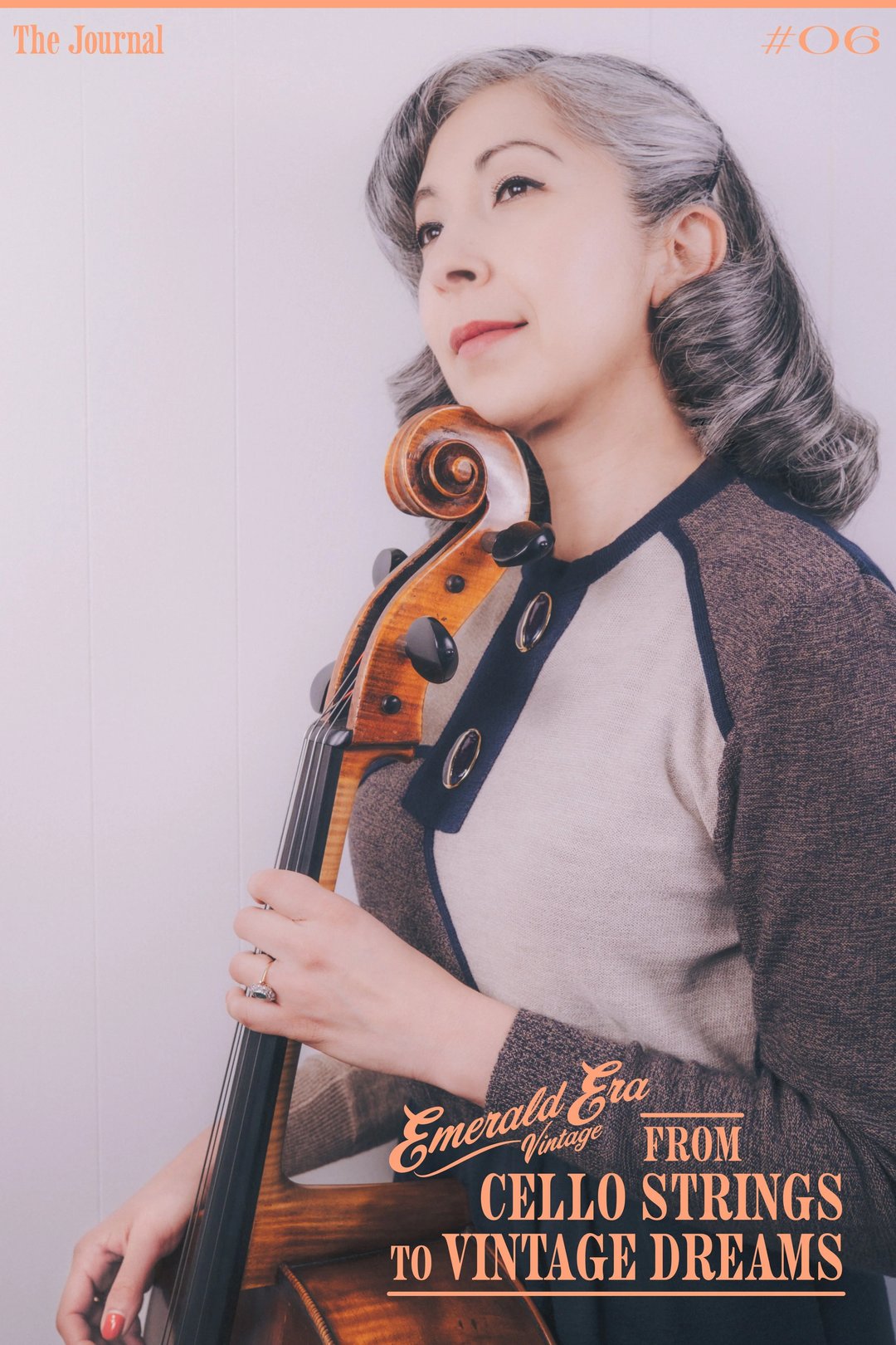 A woman with wavy gray hair holds a violin against a light background, wearing a stylish gray and black outfit.