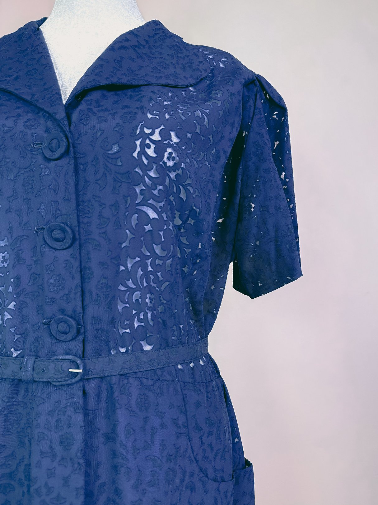 Navy blue 1940s women's dress featuring a collared neckline, short sleeves, decorative detailing, and a belted waist.