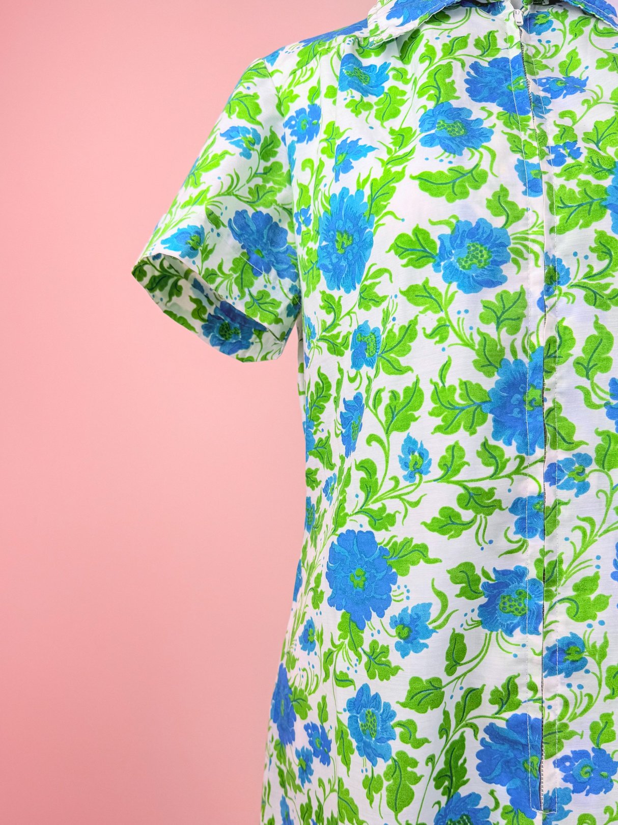 A short-sleeved, white dress with a blue and green floral pattern, reflecting a 1960s style.