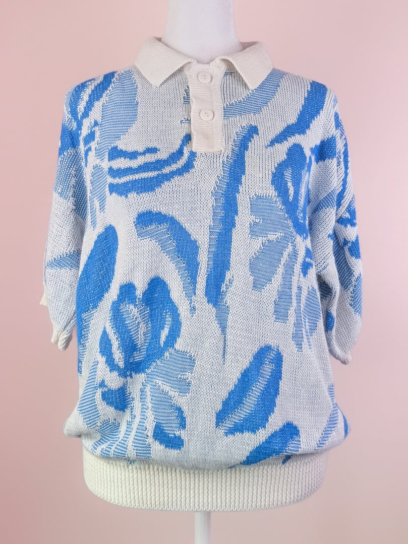 White and blue floral patterned 1980s women's knit polo sweater with a collar and short sleeves.