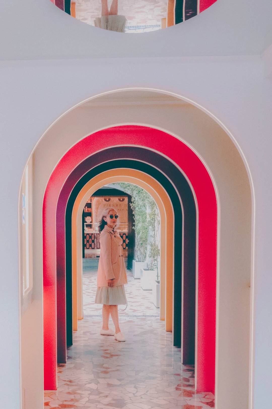 A person wearing a stylish outfit stands in an arched passageway with colorful lighting.
