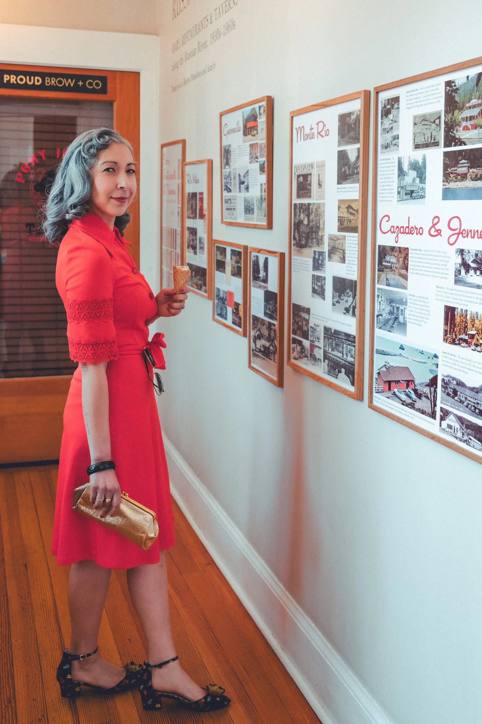 A woman in a red dress stands by a wall showcasing historical photographs and information about local landmarks.