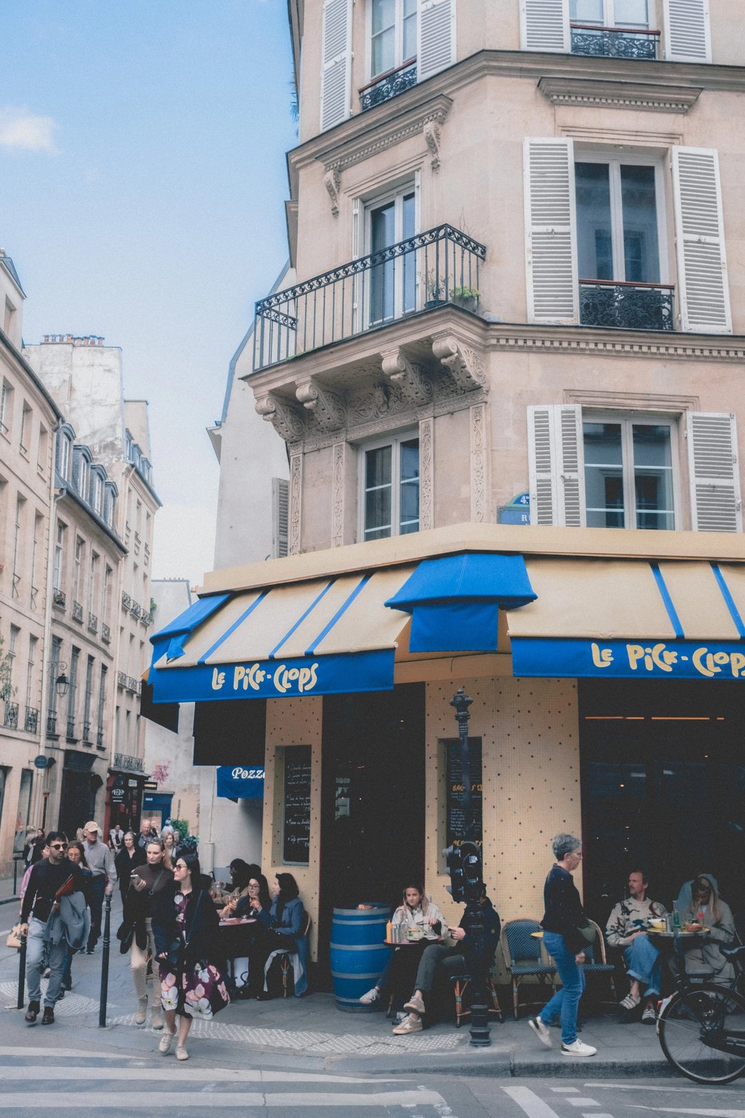 A bustling Parisian street corner featuring a café with outdoor seating under a yellow awning.