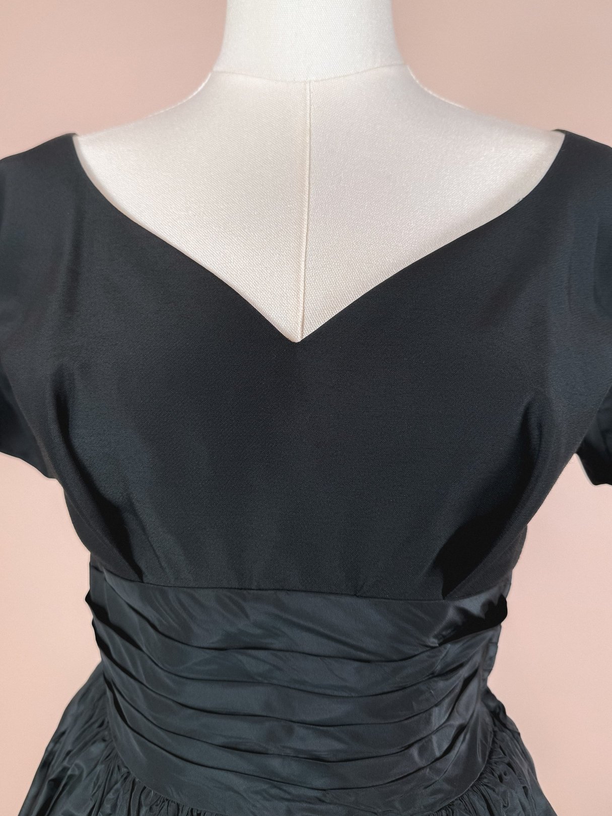 Black women's dress from the 1950s featuring a V-neckline and gathered detailing at the waist.