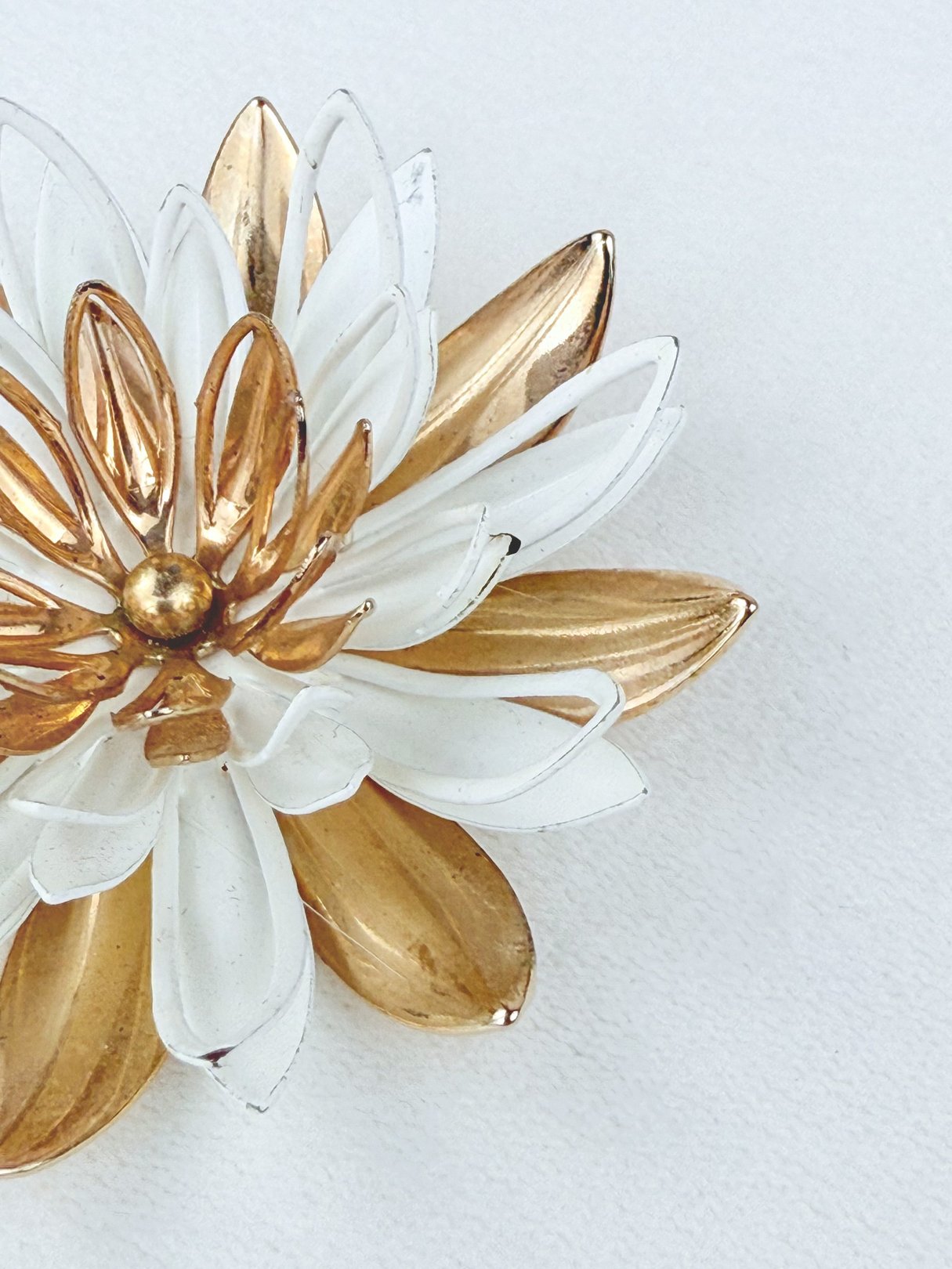 A 1950s-inspired brooch designed as a dahlia flower, featuring gold and white petals.