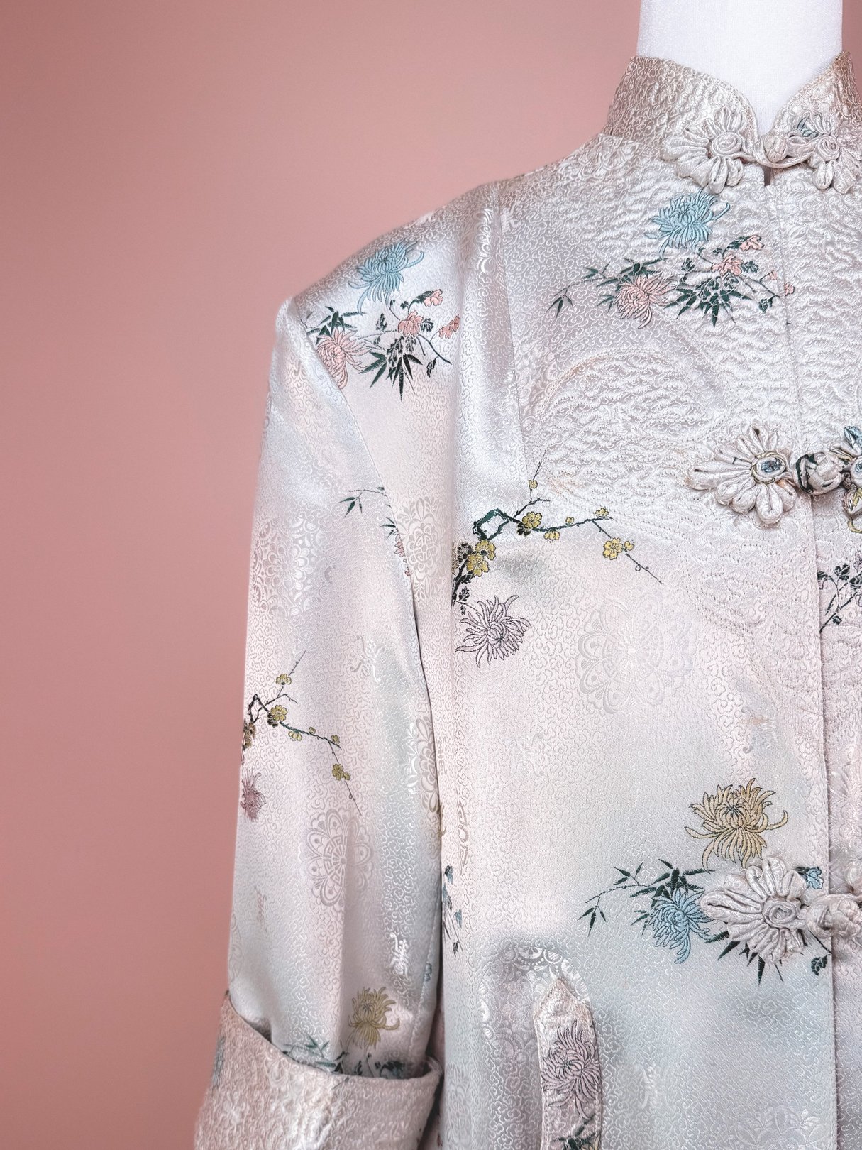 Silver 1970s women's cheongsam coat with intricate floral embroidery and traditional button closures.