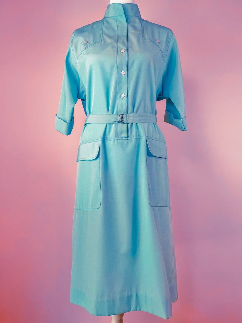 Skyline Shift Dress in sky blue featuring a collared neckline, short sleeves, a belted waist, and front pockets, styled in a 1960s design.