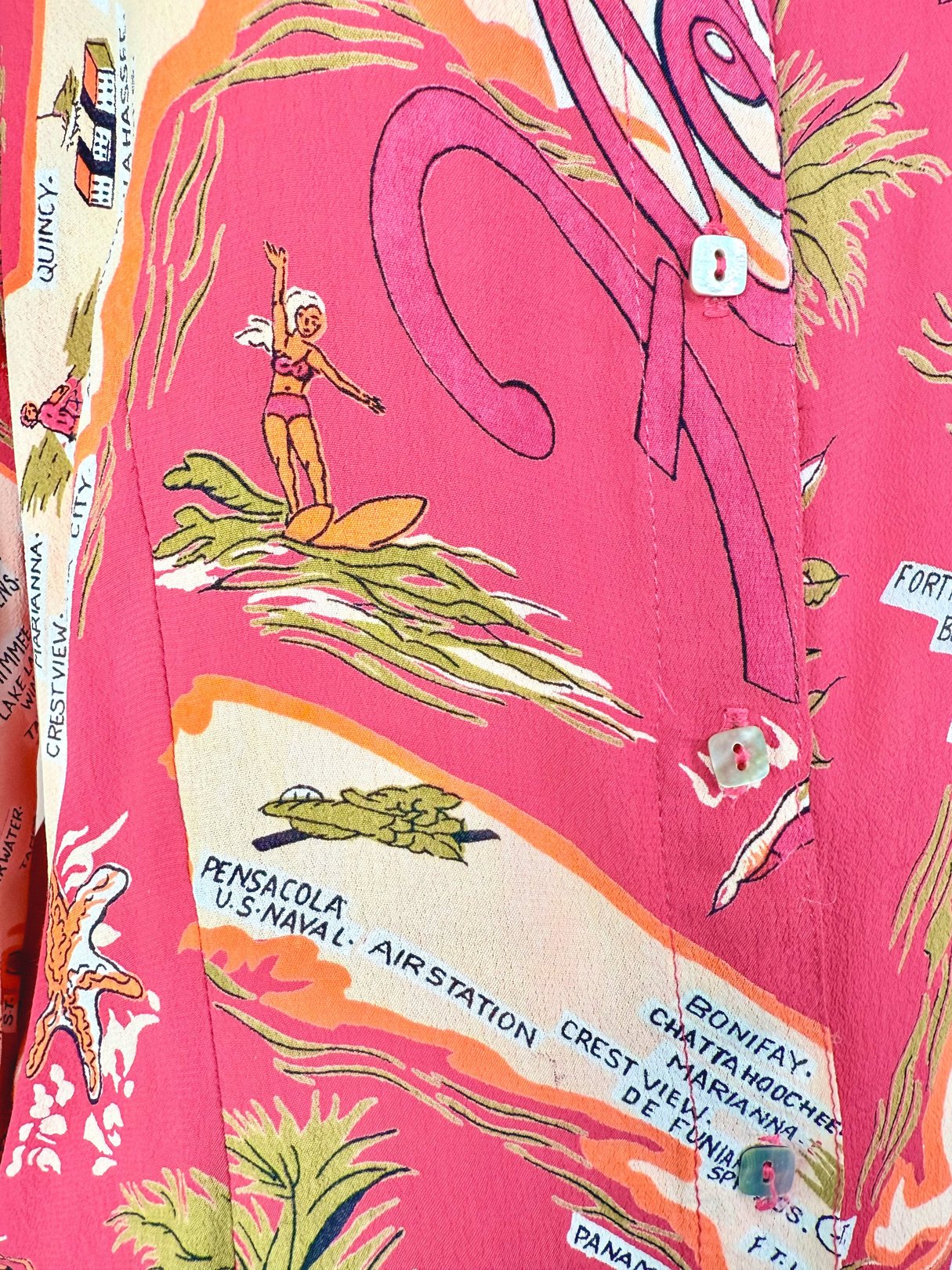 White women's top from the 1970s with a vibrant pink tropical print featuring surfing imagery and map details.