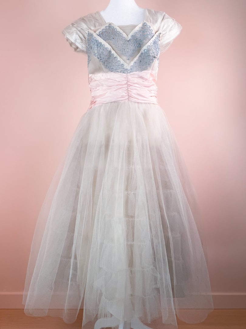 Silver 1950s-style women's dress featuring a fitted bodice with blue embellishments and a pink satin waistband, complemented by a full tulle skirt.