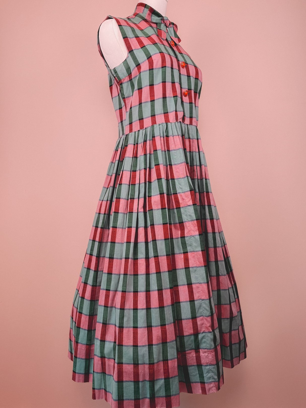 A red and green plaid dress with a pleated skirt, designed for women in a 1950s style.